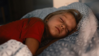 Child sleeping in bed at late night. Cute toddler girl pillow covered with warm blanket. Kid having night rest. Light on night table